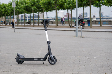 Selected focus at E-scooter or Electric Scooter by startup company with concept of Eco friendly mobility urban lifestyle, park on promenade along riverside of Rhine River in Düsseldorf, Germany.