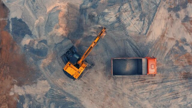Aerial top down view of an excavator loading crushed stone into a dump truck