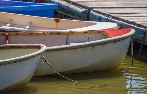 four small row boats tied to a weathered wooden pier on a sunny day