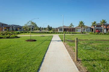 A pedestrian walkway/footpath leads to a residential neighbourhood with some modern Australian homes. Suburban view over a park with houses in the distance. Melbourne VIC Australia.