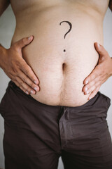 Overweight man touching his obese belly with question mark with hands. Weight loss, dieting, health care concept