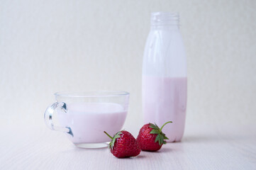 Red strawberries, yogurt in a bottle and glass mug on the table