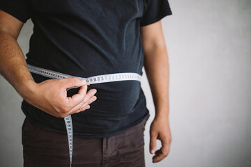 Overweight man measuring waist with measure tape, close up image. Weight loss, motivation, fat burning