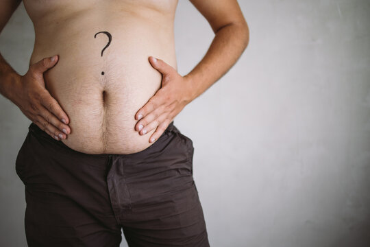 Overweight man touching his obese belly with question mark with hands. Weight loss, dieting, health care concept