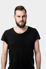 Fototapeta premium An image of a serious-looking handsome caucasian man looking towards the camera wearing a black shirt alone on white background.