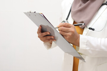 Anonymous muslim female doctor wearing hijab with stethoscope in white coat holding clipboard, ready to serve her medical patient, write medical record