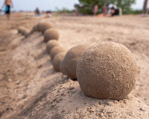 Fototapeta na wymiar Close up view of an undulating sand castle hill or wall with perfectly smooth round balls or spheres of wet sand placed on serpentine shaped ridge as people crowd the beach beyond.