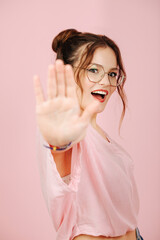 Eccentric overly happy young woman in glasses with two buns on her head over pink. She's making...