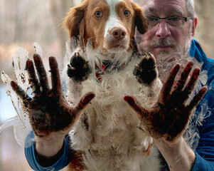 Man and dog both with dirty pand and hand prints on window. Man's best freind