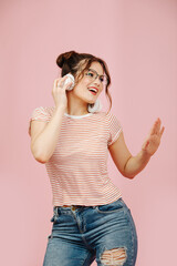 Emotional stilish woman in glasses dancing, while listening to headphones. She's wearing striped shirt and jeans. Her hair in two buns.