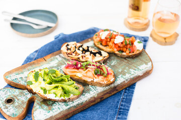 Bruschetta, crostinni, toasts with different toppings on a wood board with rose wine