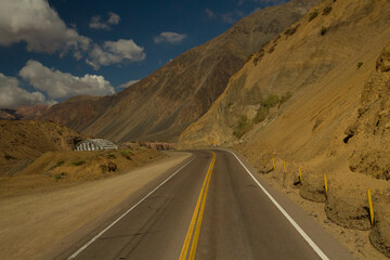 Traveling along the asphalt highway in the arid desert and mountains. The straight road ends in a curve that leads into a bridge. 