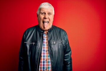 Senior handsome hoary man wearing casual shirt and jacket over isolated red background sticking tongue out happy with funny expression. Emotion concept.
