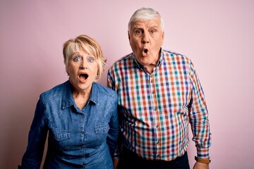 Senior beautiful couple standing together over isolated pink background afraid and shocked with surprise expression, fear and excited face.