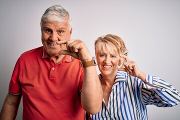 Senior beautiful couple standing together over isolated white background smiling and confident gesturing with hand doing small size sign with fingers looking and the camera. Measure concept.