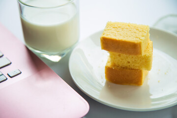 Close up a butter cake pack in a white plate next to a pink laptop device with a cup of milk blurred background in the afternoon.