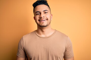 Young handsome man wearing casual t-shirt standing over isolated yellow background with a happy and cool smile on face. Lucky person.