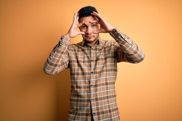 Young handsome man wearing casual shirt standing over isolated yellow background Trying to open eyes with fingers, sleepy and tired for morning fatigue