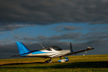 Light small plane on the grass on a background of blue clouds
