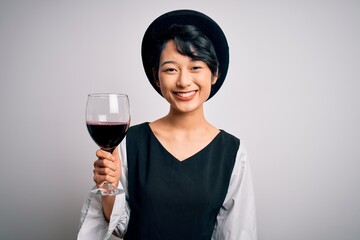 Young beautiful asian sommelier girl drinking glass of red wine over isolated white background with a happy face standing and smiling with a confident smile showing teeth