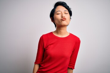 Young beautiful asian girl wearing casual red t-shirt standing over isolated white background looking at the camera blowing a kiss on air being lovely and sexy. Love expression.