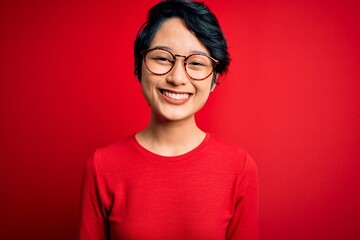 Young beautiful asian girl wearing casual t-shirt and glasses over isolated red background with a happy and cool smile on face. Lucky person.