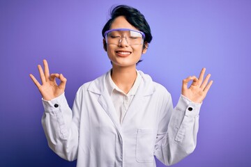 Young beautiful asian scientist girl wearing coat and glasses over purple background relax and smiling with eyes closed doing meditation gesture with fingers. Yoga concept.