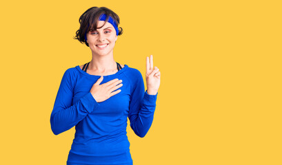 Beautiful young woman with short hair wearing training workout clothes smiling swearing with hand on chest and fingers up, making a loyalty promise oath