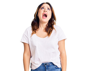 Obraz premium Young beautiful caucasian woman wearing casual white tshirt angry and mad screaming frustrated and furious, shouting with anger. rage and aggressive concept.