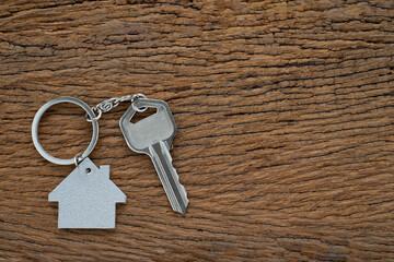 Silver key house with house shaped keychain on vintage wooden table background. 