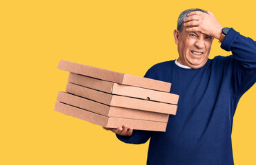 Senior handsome man holding pizza boxes stressed and frustrated with hand on head, surprised and angry face