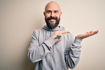 Obraz premium Handsome sporty bald man with beard wearing sweatshirt standing over pink background amazed and smiling to the camera while presenting with hand and pointing with finger.