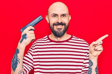 Young handsome man holding gun smiling happy pointing with hand and finger to the side