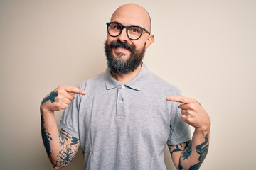 Handsome bald man with beard and tattoo wearing casual polo and glasses looking confident with...