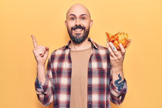 Young handsome man holding nachos potato chips smiling happy pointing with hand and finger to the side