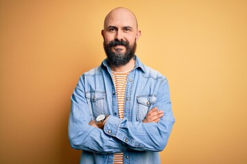 Handsome bald man with beard wearing casual denim jacket and striped t-shirt happy face smiling with crossed arms looking at the camera. Positive person.