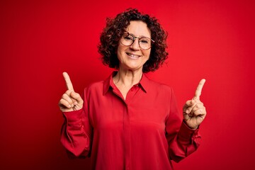 Middle age beautiful curly hair woman wearing casual shirt and glasses over red background smiling...