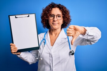 Middle age curly hair doctor woman wearing coat and stethoscope holding clipboard with angry face,...