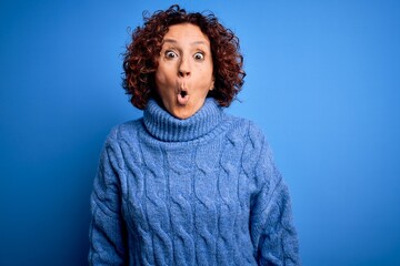 Fototapeta premium Middle age beautiful curly hair woman wearing casual turtleneck sweater over blue background afraid and shocked with surprise expression, fear and excited face.