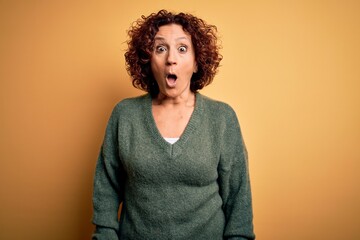 Fototapeta na wymiar Middle age beautiful curly hair woman wearing casual sweater over isolated yellow background afraid and shocked with surprise expression, fear and excited face.