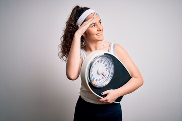 Young beautiful woman with curly hair holding weighing machine over white background very happy and...