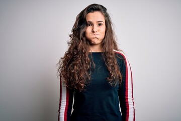 Young beautiful woman with curly hair wearing casual sweater over isolated white background puffing cheeks with funny face. Mouth inflated with air, crazy expression.