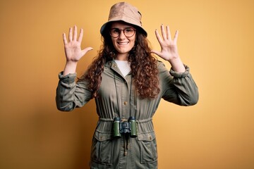 Young beautiful tourist woman on vacation wearing explorer hat and binoculars showing and pointing...