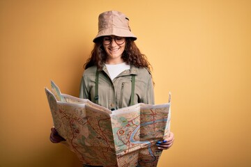 Beautiful tourist woman on vacation wearing explorer hat and water canteen holding city map with a happy face standing and smiling with a confident smile showing teeth