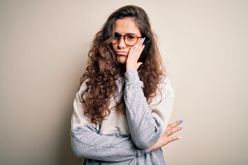 Young beautiful woman with curly hair wearing sweater and glasses over white background thinking looking tired and bored with depression problems with crossed arms.