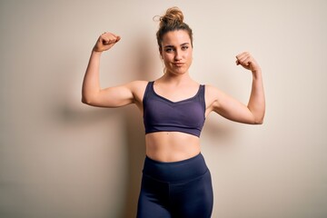 Fototapeta na wymiar Young beautiful blonde sportswoman doing sport wearing sportswear over white background showing arms muscles smiling proud. Fitness concept.