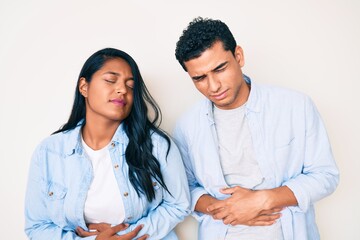 Beautiful latin young couple wearing casual clothes with hand on stomach because indigestion, painful illness feeling unwell. ache concept.