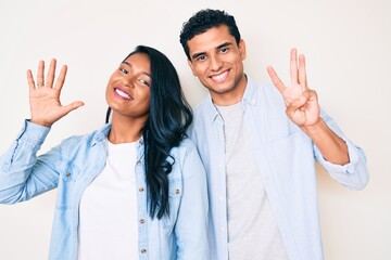 Fototapeta na wymiar Beautiful latin young couple wearing casual clothes showing and pointing up with fingers number eight while smiling confident and happy.