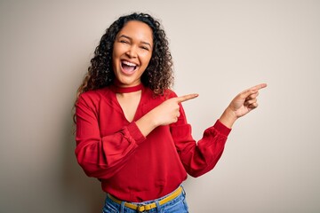 Young beautiful woman with curly hair wearing casual t-shirt standing over white background smiling and looking at the camera pointing with two hands and fingers to the side.