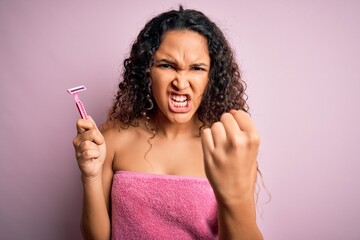 Obraz premium Young beautiful woman with curly hair wearing shower towel holding depilation razor annoyed and frustrated shouting with anger, crazy and yelling with raised hand, anger concept
